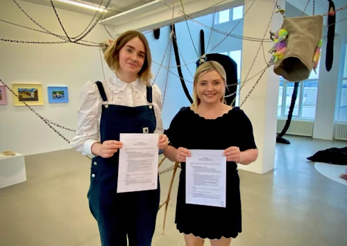 Sunna Ástþórsdóttir, safnstjóri Nýlistasafnsins, og Lilja Alfreðsdóttir, menningar- og viðskiptaráðherra, halda á samningnum í sýningarsal safnsins í Marshallhúsinu.